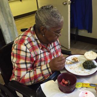An elderly woman in a wheelchair enjoying a meal indoors.