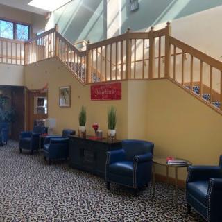 A cozy lobby area with blue chairs, a patterned carpet, and a wooden staircase leading to an upper level.