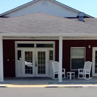 A small building with a porch featuring rocking chairs and glass doors.