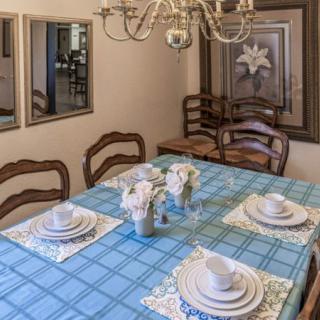 A neatly arranged dining room featuring a table with a blue checkered tablecloth, set with white dishes and a floral centerpiece under an elegant chandelier.
