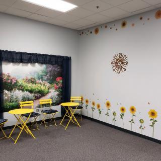A cozy indoor seating area featuring bright yellow chairs and a garden-themed wall with sunflowers and a scenic mural.