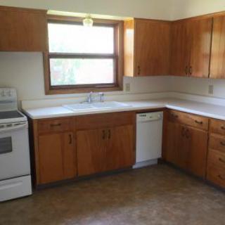 A kitchen with wooden cabinets, a stove, dishwasher, and a window.