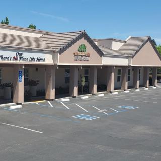 A row of storefronts in a strip mall with an adjacent parking lot on a sunny day.