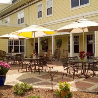 A sunny patio with tables and chairs under umbrellas in front of a yellow building.