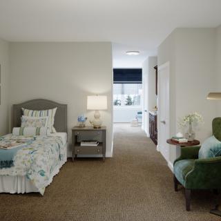 A cozy bedroom with a single bed and comfortable armchair, featuring soft lighting from a bedside lamp.