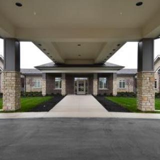 A modern building entrance featuring a covered walkway with a stone facade and surrounding landscaping.