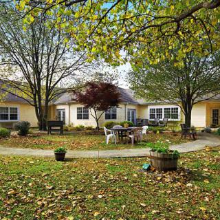 A peaceful garden setting with chairs and a pathway surrounded by autumn foliage.