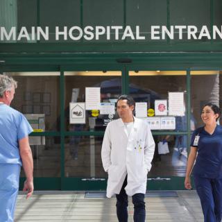 Medical staff walking in front of the main hospital entrance.