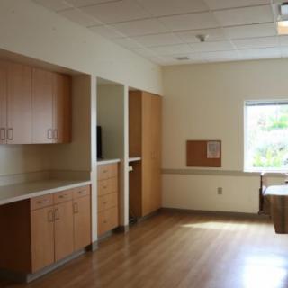 An empty hospital room with built-in cabinets and a large window letting in natural light.