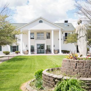 A stately building with tall columns and a well-maintained lawn, featuring a prominent statue in the foreground.