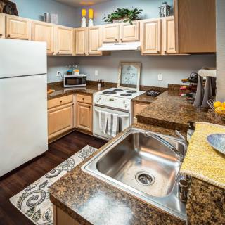 A modern kitchen interior featuring wooden cabinets, a stainless steel sink, and various appliances including an oven and refrigerator.