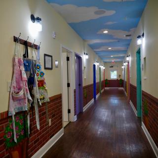 A vibrant hallway with colorful doors, an artistic sky-themed ceiling, and aprons hanging on the wall.