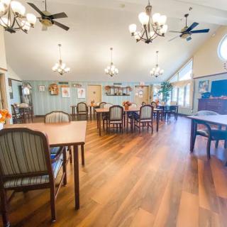 A spacious dining area with wooden flooring, featuring several tables and chairs, elegant chandeliers, and ceiling fans.