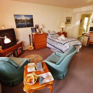 A cozy bedroom with comfortable armchairs, a bed, and a guitar by the television.