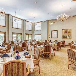 A spacious and elegantly decorated dining room featuring neatly arranged tables and chairs, illuminated by chandeliers.
