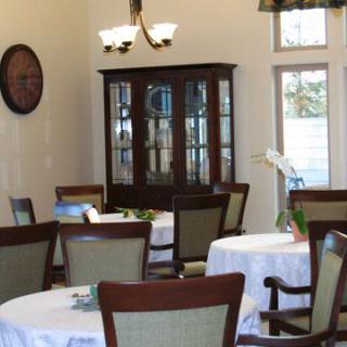 A cozy dining room with neatly arranged tables and chairs, featuring a cabinet and a wall clock.