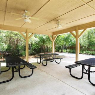 A spacious outdoor pavilion featuring picnic tables and ceiling fans, surrounded by greenery.