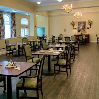 An elegant dining room setup with neatly arranged tables and chairs, illuminated by chandeliers.