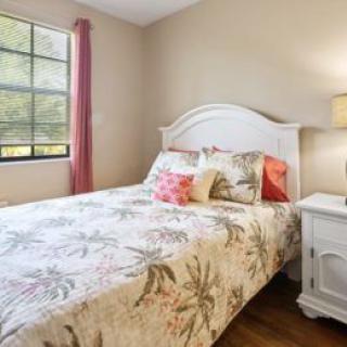 A cozy bedroom with a floral bedspread, white headboard, and a warm lamp on the nightstand.