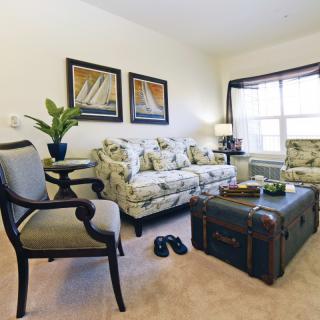A cozy living room with floral-patterned furniture, a trunk-style coffee table, and decorative elements like plants and artwork.
