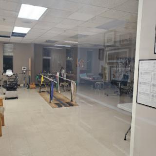 A view of a rehabilitation gym featuring exercise equipment and a glass partition.