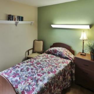 A cozy bedroom with a floral bedspread, a lamp on the side table, and a chair against the wall.