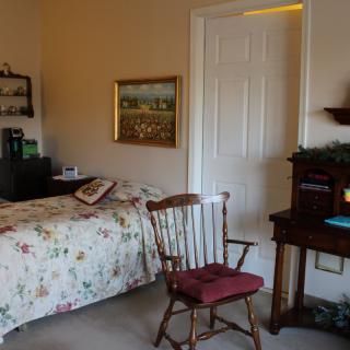 A cozy bedroom with a wooden chair, desk, and a bed adorned with floral bedding.