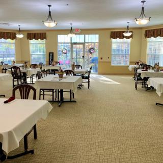 Spacious dining area with neatly arranged tables and chairs, illuminated by natural light from large windows.