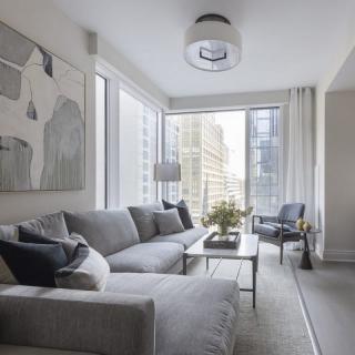 A modern living room with a gray sofa and large windows showcasing a city view.