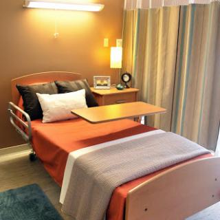 A cozy hospital room featuring a bed, bedside table, and soft lighting.