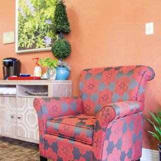 A cozy corner with a patterned armchair and a coffee station against an orange wall.