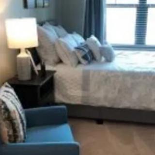 Cozy bedroom with a neatly made bed, pillows, lamp, and chair by the window.
