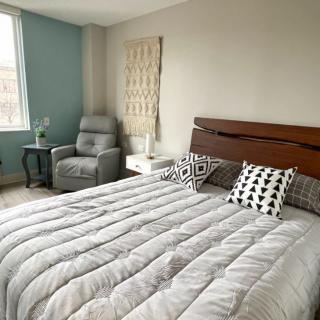 A modern and minimalist bedroom with a comfortable bed, stylish pillows, and an armchair by the window.