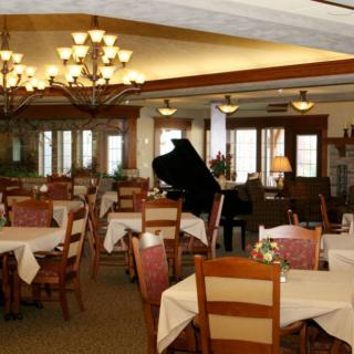 An elegant restaurant dining area with a piano, decorated with chandeliers and set tables.