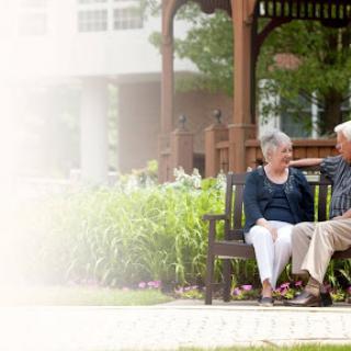 An elderly couple enjoying a moment together on a bench in a serene park setting.