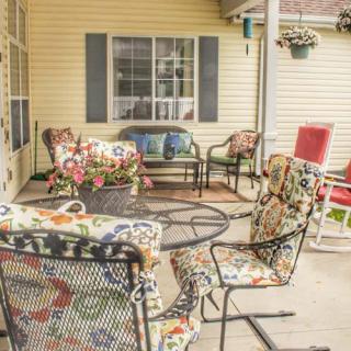 A cozy outdoor patio area with various chairs and a table, featuring colorful cushions and a hanging flower pot.