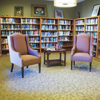 A cozy library reading area with two chairs and a small table surrounded by bookshelves.