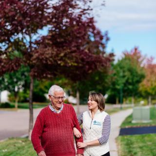 An elderly man walking with a caregiver on an autumn day.
