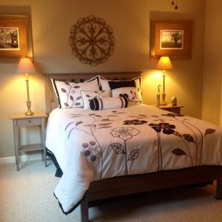 A cozy bedroom featuring a neatly made bed with decorative bedding, accompanied by warm lighting from lamps on side tables and wall art completing the decor.