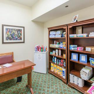 An office space with a desk, bookshelves filled with supplies, and a small refrigerator.