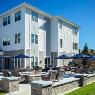 A modern residential building with outdoor seating and umbrellas on the patio.