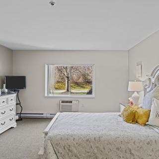 A cozy bedroom with neutral tones featuring a bed, dresser, and window view.