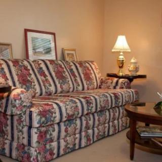 A cozy living room with a floral patterned sofa, lamp, and artwork on the walls.