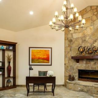 A cozy living room with a stone fireplace, chandelier, and a desk.