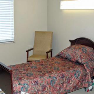 A simple room featuring a single bed, a chair, and a window with blinds.
