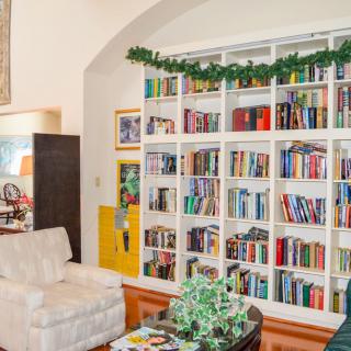 A cozy living room featuring a white armchair and a large bookshelf filled with books, adorned with a festive garland.