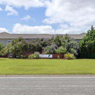 A building with a well-maintained lawn and a sign in front, surrounded by trees under a partly cloudy sky.