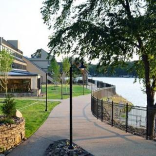 A scenic pathway running alongside a lake with trees, a building, and a lamppost.