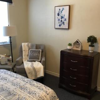 A cozy bedroom corner with a chair, dresser, and decorative items.