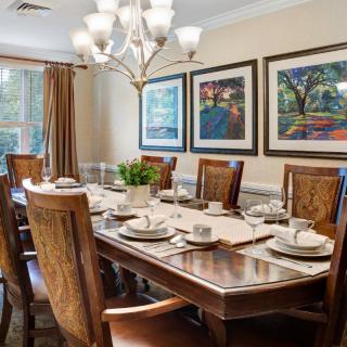 A well-appointed dining room featuring a large wooden table set for a meal, surrounded by matching chairs, with a chandelier hanging overhead and framed artwork on the walls.